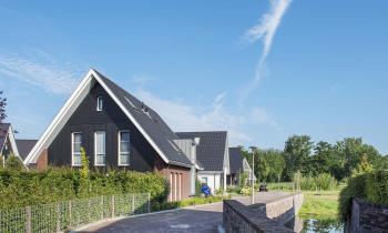 Een weg langs een heg die loopt aan het water waar woningen aan grenzen